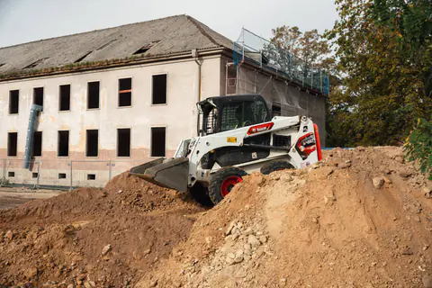 Kompaktlader verteilt Erdaushub vor einem Altbau in Potsdam-Krampnitz