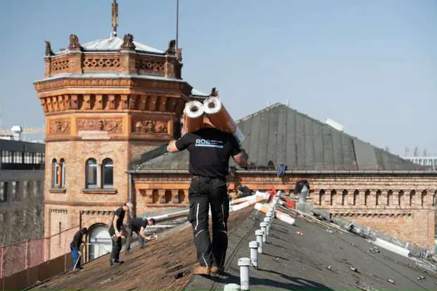Dachsanierung Potsdam: Dachdecker auf dem Steildach vor historischem Turm